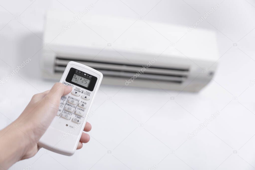 Close-up of men hand operating air conditioner with remote control, Close up shot of hand holding the remote control of  white air conditioner on white color wall.