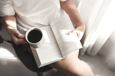 Kitap okuyan ve elinde bir fincan kahve olan genç kadınlar dinlenmenin keyfini çıkarıyorlar, kız kitap okuyor.