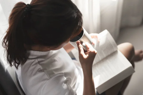 Kitap okuyan ve elinde bir fincan kahve olan genç kadınlar dinlenmenin keyfini çıkarıyorlar, kız kitap okuyor.