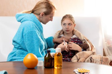 Bir kadın bir kıza termometre yerleştirir. Termometresi olan anne..