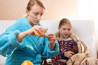 Annem öksürük şurubu döker. Annem kızına bakıyor..