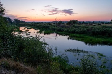 Nehrin üzerinde gün batımı. Tarlada küçük bir nehir.