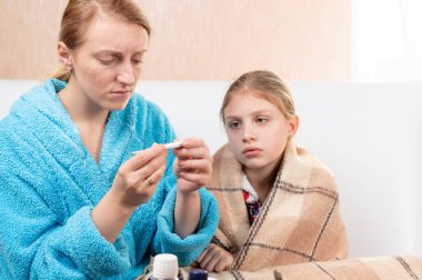 Bir kadın hasta bir çocuğun sıcaklığını ölçer. Anne kızının sıcaklığını ölçer..