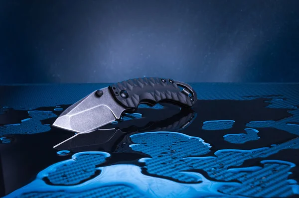 Cuchillo con hoja negra y mango sobre fondo azul. Cuchillo en el agua. Reflejo de un cuchillo en el agua . — Foto de Stock