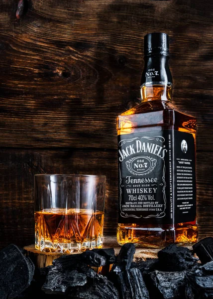 Kyiv, Ukraine - march 11, 2020: Bottle of whiskey and a glass of whiskey Jack Daniels. Whiskey on a wooden background and charcoal. — Stock Photo, Image