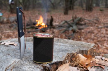 Teneke kutu ve şenlik ateşinde bıçak. Teneke kutuda yemek ve bıçak. Konserve yiyecekleri bıçakla aç. Doğada yemek..