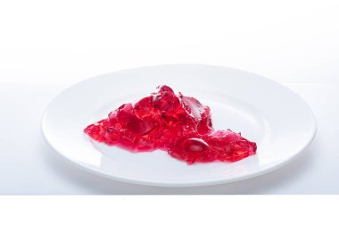 Beyaz bir tabakta kırmızı şekilsiz jöle. Beyaz arka planda kırmızı jöle. Jöleyi ayır. Üst.