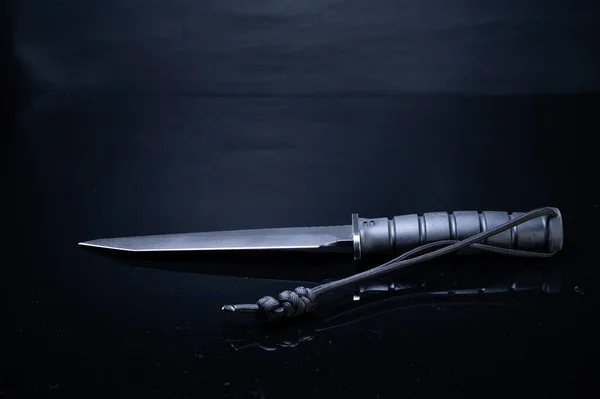 Large army knife on a black background. Black knife on a black foe. Military knife with a lanyard. The knife lies on the table.