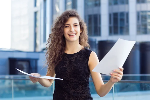 Ragazza riccia che tiene in mano una carta sullo sfondo del business center, sorridendo — Foto Stock