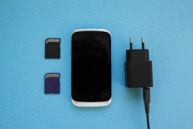 Belgili tanımlık smartphone, iki hafıza kartı ve şarj mavi bir arka plan üzerinde.