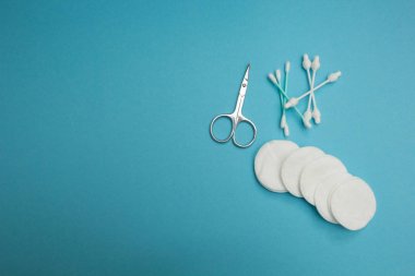 Makas, pamuk temizleme bezi ve mavi bir arka plan üzerinde yastıkları
