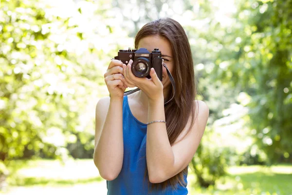 Chica sosteniendo una cámara y tomando fotos en el parque sobre un fondo de árboles — Foto de Stock