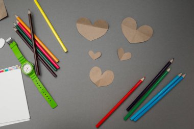 Kağıt kalpleri ve gri arka plan üzerinde renkli kalemler