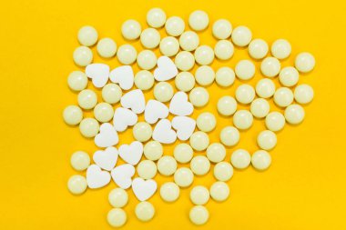 Sarı bir arka plan üzerinde kalp şeklinde dağınık hapları