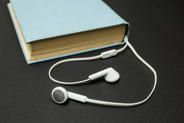 Old blue book, and white headphones on a black background — Stock Photo, Image