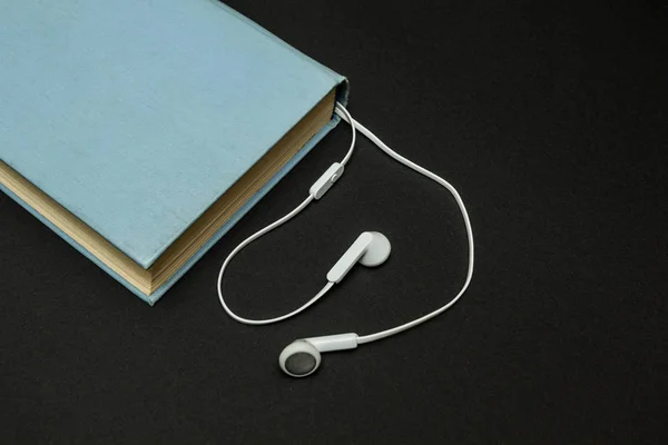 Libro azul viejo, y auriculares blancos sobre un fondo negro — Foto de Stock