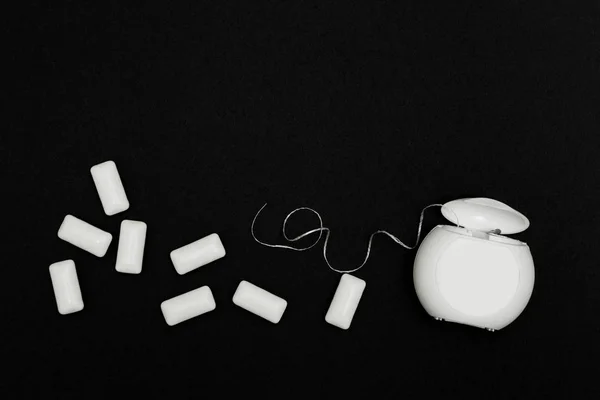 Almohadillas de goma de mascar y hilo dental sobre fondo negro . — Foto de Stock
