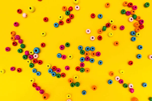 Spilled multi-colored beads on a yellow background.