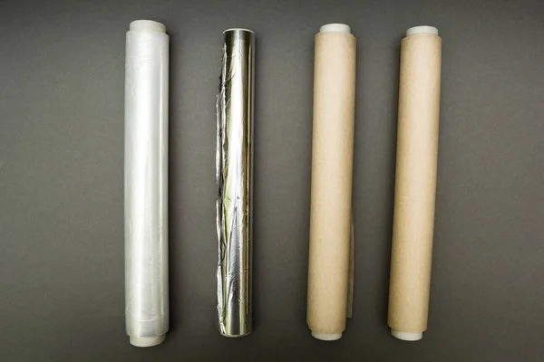 Envoltura de plástico, papel de aluminio y rollo de papel pergamino sobre gris — Foto de Stock