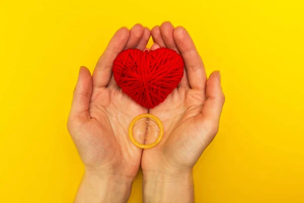 Kondom und rotes Herz in den Händen auf gelbem Hintergrund. — Stockfoto