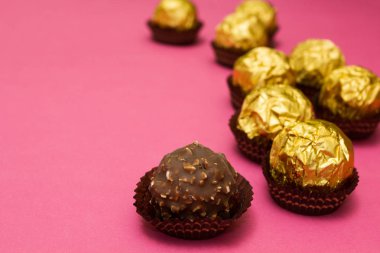 Altın bir sarmalayıcı üzerinde pembe bir arka plan, metin için yer yer çikolata tatlılar.