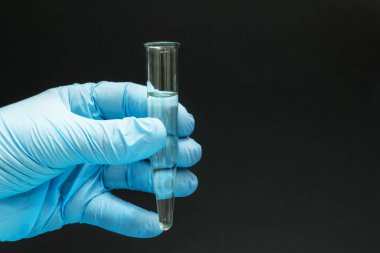 Bir cam tüp siyah bir zemin üzerine bir homeopatik ilaç mavi eldiven elinde tutan yakın çekim.
