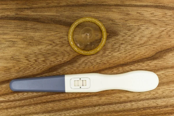 Позитивний тест на вагітність і презерватив на дерев'яному тлі, дві смужки . — стокове фото