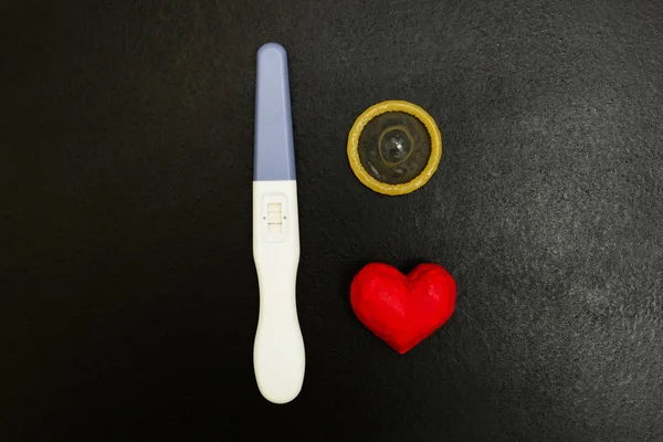 阳性妊娠试验和避孕套的木质背景, 两条和一颗红色的心. — 图库照片