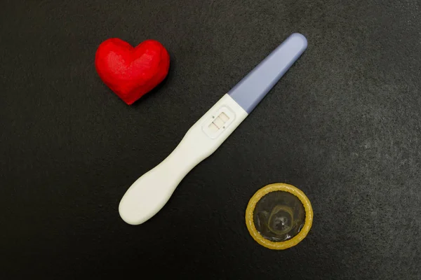 Positive pregnancy test and condom on a wooden background, two strips and a red heart. — Stock Photo, Image