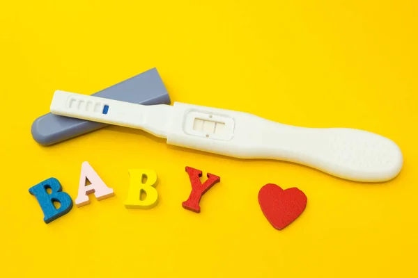 Позитивний тест на вагітність, серце і слово "дитина" на жовтому тлі . — стокове фото