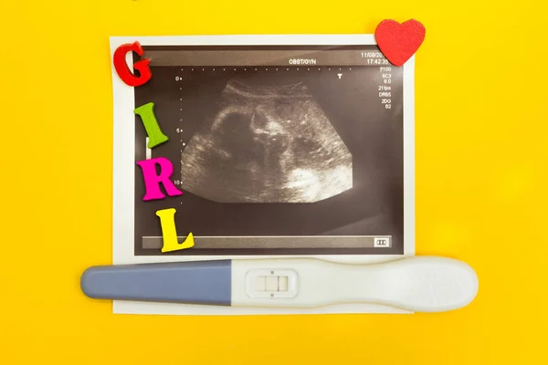 Позитивний тест на вагітність, ультразвукова фотографія, червоне серце і слово "дівчина" на жовтому тлі . — стокове фото