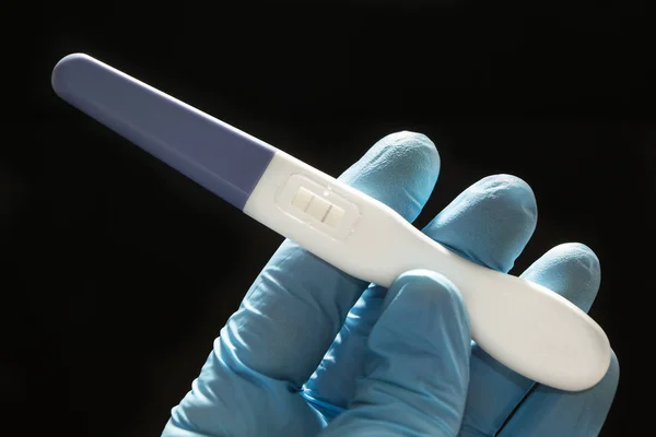 Positive pregnancy test with two strips in the hand in a blue medical glove on a black background. — Stock Photo, Image