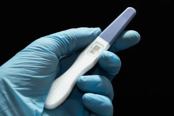Positive pregnancy test with two strips in the doctor's hand in a blue medical glove against a black background. — Stock Photo, Image