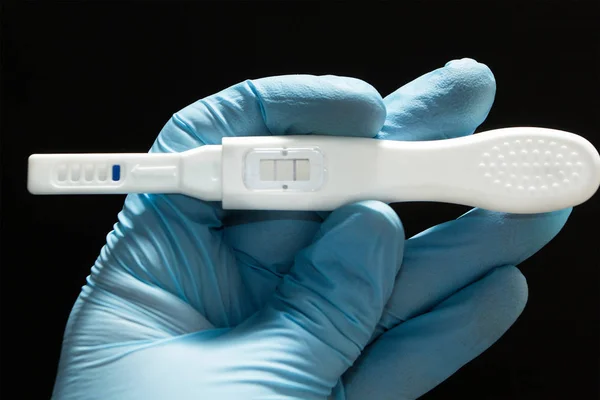 Successful artificial insemination. Positive pregnancy test with two strips in the hand in a blue medical glove on a black background. — Stock Photo, Image