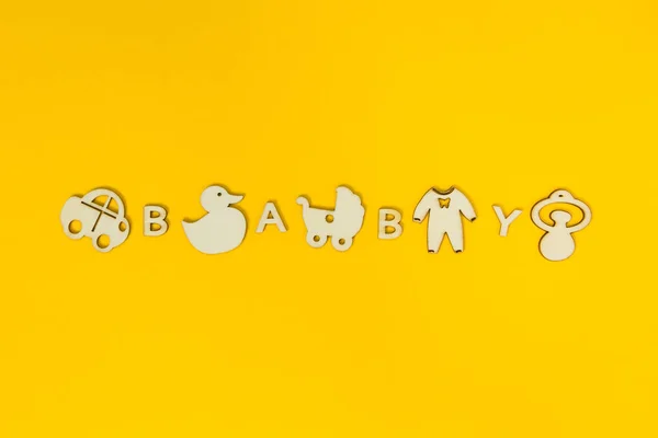 A palavra "bebê" em um fundo amarelo foi misturada com figo de madeira — Fotografia de Stock