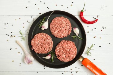 Sarımsak, biberiye ve biber ile beyaz bir arka plan üzerinde organik sığır eti ham beşamel sos bir kızartma içinde baharatlar ile pan. Üstten görünüm.