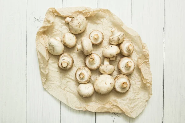 Farmer\'s mushrooms champignons on parchment paper. Organic vegetables on a white wooden background.