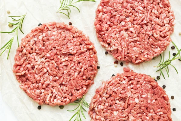 Raw hamburgers without fat from organic beef on a white wooden background with spices. Nourishing food. Top view.