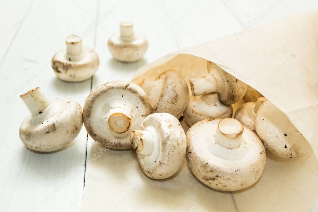 Freshly picked farm mushrooms champignons on a white wooden background in a paper bag. Organic vegetables.
