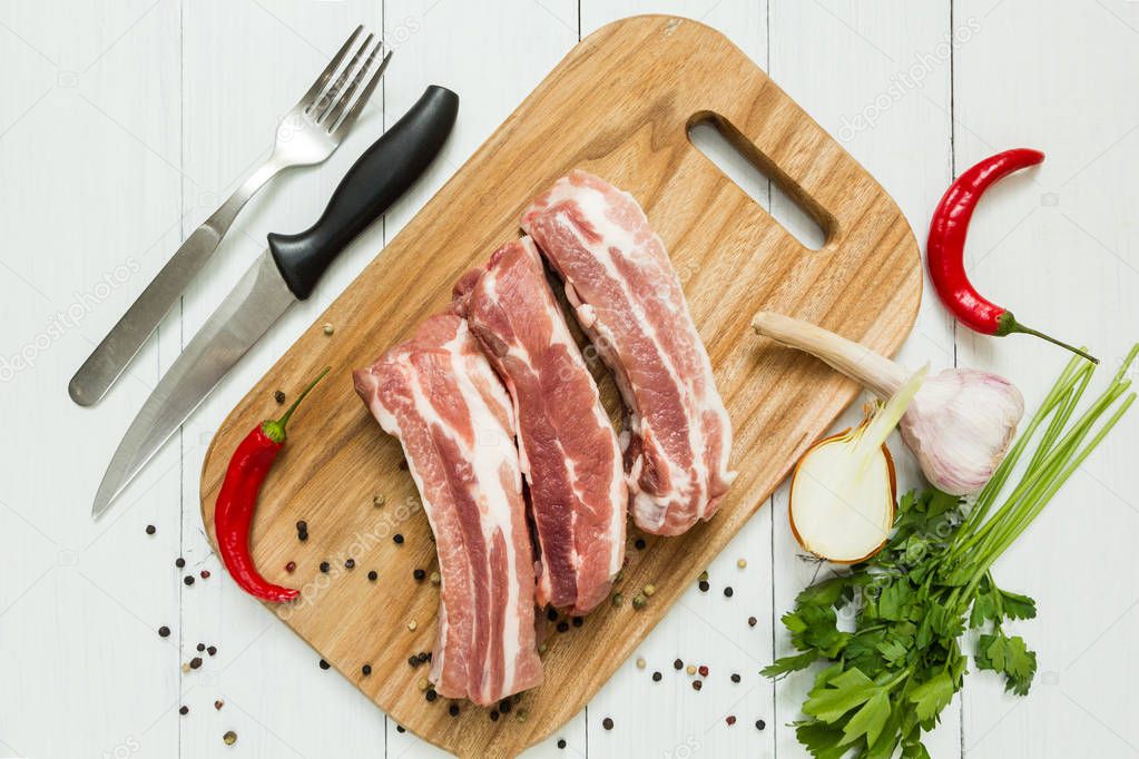 Raw pork ribs with vegetables and pepper on a cutting board. Knife and fork. Top view.