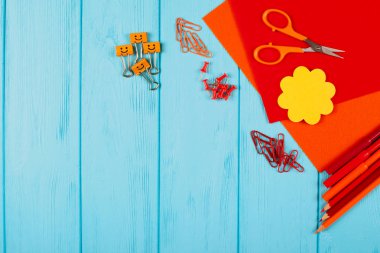 Kırmızı ve turuncu kalemler, keçeli kalemler, notepaper, ataç, ileti örneği çivi, hissettim ve mavi ahşap arka plan için makaslar