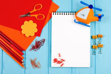 Kırmızı ve turuncu kalemler, keçeli kalemler, notepaper, ataç, ileti örneği çivi, hissettim ve mavi ahşap arka plan için makaslar