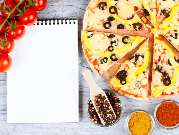 Horizontal food banner with cherry tomatoes, cut pizza, spice and notebook on wooden background. Empty space for text