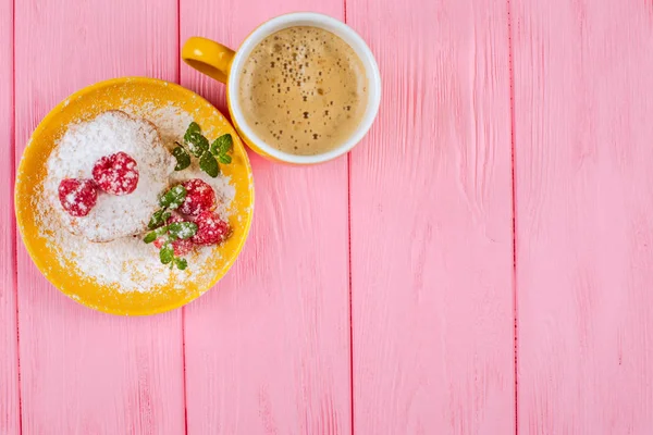 Homemade baked muffin with raspberries, fresh berries, mint on plate and cup of coffee on pink wooden background.