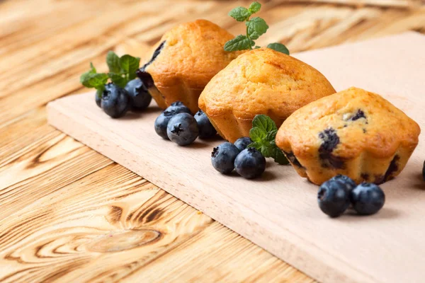 Homemade baked muffin with blueberries, fresh berries, mint on wooden background. Empty space for text.