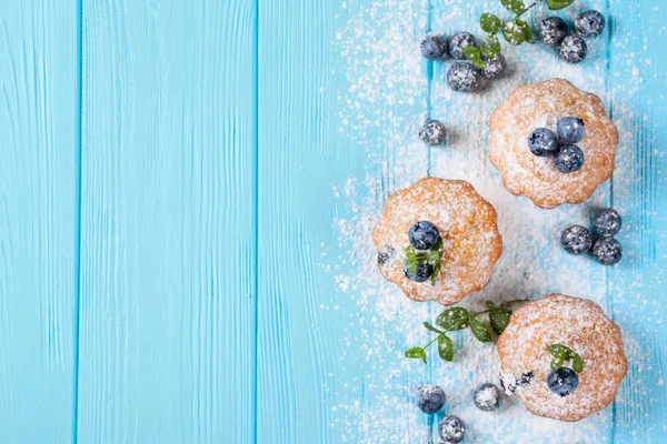 Homemade baked muffin with blueberries, fresh berries, mint, powdered sugar on blue wooden background. Top view.