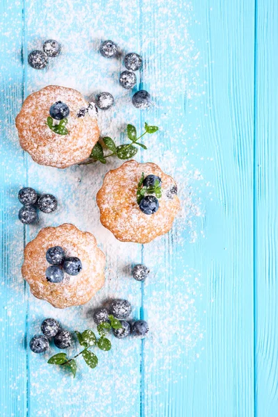 Homemade baked muffin with blueberries, fresh berries, mint, powdered sugar on blue wooden background. Top view.