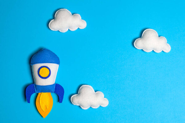 Rocket takes off. Space ship with white clouds on blue background. Hand made felt toys.