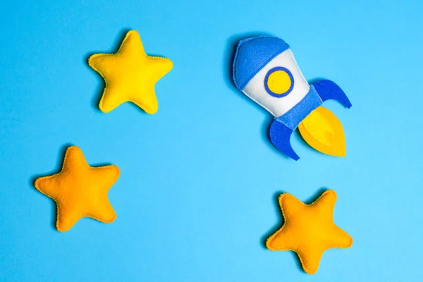Rocket takes off. Hand made felt toys. Space ship with yellow stars on blue background.