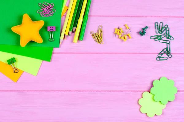 Lápices amarillos y verdes, rotuladores, bloc de notas, clips de papel, clavos de papelería, fieltro y sonrisas sobre fondo de madera rosa —  Fotos de Stock
